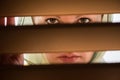 Lonely muslim young woman in a headscarf with frightened eyes looks through the wooden blinds. Concept.