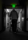 A lonely old man, leaning on a walker, walks in a dark corridor under the sign of an exit. Concept, old age, loneliness