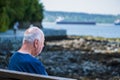 A lonely old man sitting on a bench in a park. Back view of an elderly sad man sitting on a bench Royalty Free Stock Photo