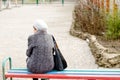 A lonely old woman sits on a bench in a park