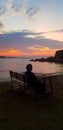 Lonely old woman in the evening sitting on a bench on the beach and watching the beautiful sunset Royalty Free Stock Photo