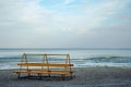 Lonely orange bench on the shore of a calm blue sea with a ship on the horizon. Royalty Free Stock Photo