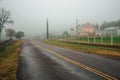 Lonely paved road with houses in a foggy day