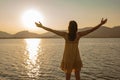 Lonely pensive woman with open arms in adoration of sun reflecting in ocean sea water at sunset or sunrise. Concept of Royalty Free Stock Photo