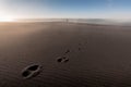Lonely person silhouette standing far in background and footprints on the sand Royalty Free Stock Photo