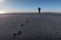 Lonely person silhouette standing far in background and footprints on the sand Royalty Free Stock Photo