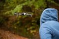 Selective focus shot of a mysterious man in a hoodie examining a flying drone in front of him