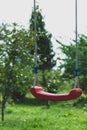 Lonely red hanging swings in green garden background Royalty Free Stock Photo