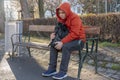 Lonely and sad guy 25-30 years old with a backpack in the park on a bench, blurred urban background. Concept: a homeless man on th Royalty Free Stock Photo