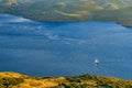 Lonely sailboat or yacht navigating in Aegean sea near Milos island on sunset. Distant hills, high coast, low sun Royalty Free Stock Photo