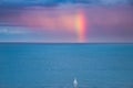 Sport, travel and leisure: A lonely sailing boat in Dublin bay on the Atlantic Ocean at dusk with a rainbow on the horizon