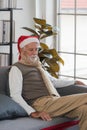 Lonely senior man in Santa hat sitting on sofa indoors at Christmas. sad and bored senior man thinking at home in winter. Royalty Free Stock Photo