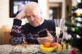 lonely senior man sitting at home table during Christmas holidays, looking at phone Royalty Free Stock Photo