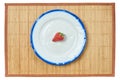Lonely strawberry on a white plate with a blue rim on a cane place mat Royalty Free Stock Photo