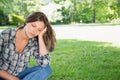 Teenage girl sitting cross-legged on grass in park, leaning head on hand under sunlight, copy space Royalty Free Stock Photo