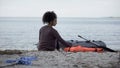 Lonely teenage girl sitting near boat, shipwreck survivor on desert island