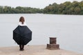 Lonely teenage girl with umbrella standing on river dock in autumn