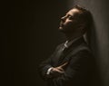 Lonely tired businessman stands closed eyes with arms crossed. Profile view of thoughtful handsome man in black suit