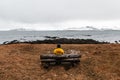 Lonely unrecognized traveler man in yellow rain jacket  is relaxing at nice view of sea and mountain with wooden bench in Reykjavi Royalty Free Stock Photo