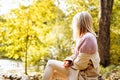 Lonely upset woman wearing cozy warm knitted sweater and coat sit in park at autumn sunny day