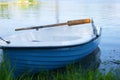 Lonely white-blue wooden boat with oars on the shore of a lake or river Royalty Free Stock Photo