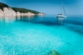 Lonely white sailing catamaran boat drift on calm sea surface. Pure shallow azure blue bay water of a beautiful beach