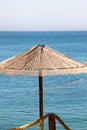 Lonely wicker sun umbrella at mediterranean beach by sea. Natural bamboo sunshades and summer umbrella parasol on ocean beach. Royalty Free Stock Photo