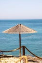 Lonely wicker sun umbrella at mediterranean beach by sea. Natural bamboo sunshades and summer umbrella parasol on ocean beach. Royalty Free Stock Photo