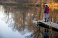 Lonely woman fishing with a rod in little village lake or pond.