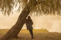 Lonely woman having rest under the tree near the water in a foggy autumn day. Lonely woman enjoying nature landscape in autumn Royalty Free Stock Photo