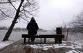 Lonely woman sits on a bench on wood flooring on a winter day and looks at the river Royalty Free Stock Photo