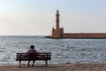 A lonely woman sitting on a bench in the old port and looking at the old lighthouse