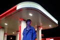 Lonely woman standing against petrol station in red neon light at night, waiting for car to refuel Royalty Free Stock Photo