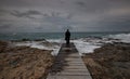 Lonely woman standing at the edge of a wooden pier in the stormy sea at sunset. Feeling free. Waves splashing on rocky Royalty Free Stock Photo