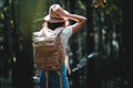 Lonely woman traveling among forest with backpack. Young traveler wearing hat and hold directional map in hand