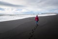 Lonely Woman Walking on a Black Sandy Beach and Cloudy Sky Royalty Free Stock Photo