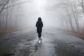 Lonely woman walking in fog away road. Rural landscape with road in morning mist. Warm autumn colors. Dark mysterious background Royalty Free Stock Photo