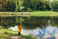 Lonely woman in yellow raincoat walking in summer park. Girl admires lake landscape view after rain Royalty Free Stock Photo