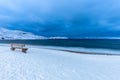 Lonely wooden bench overlooking the sea on a snow covered beach at dusk