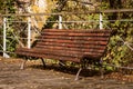Lonely wooden bench surrounded by dry fallen leaves in a quiet park in an autumn afternoon Royalty Free Stock Photo