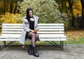 Young girl in a gray coat sits on a bench in a city park Royalty Free Stock Photo