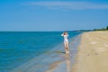 A lonely young girl in a swimsuit and sunglasses stands on the sand near the surf on an empty sea beach. Bright sunny Royalty Free Stock Photo