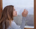 Lonely young lady looking out window, lost in thought, touching glass with rain drops Royalty Free Stock Photo