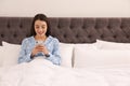 Lonely young woman addicted to smartphone in bed at home