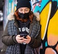 Lonely young woman chatting on her mobile phone, practicing social distance and wearing a disposable face mask as protection versu