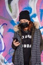 Lonely young woman chatting on her mobile phone, practicing social distance and wearing a disposable face mask as protection versu