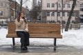 Lonely young woman sits on park bench in city and talks on phone . Girl in beige sheepskin coat rests outside in winter