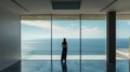 Lonely young woman stands at luxury home interior and looks at sea outside window, person and stunning amazing view from apartment Royalty Free Stock Photo