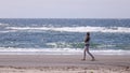 A lonely young woman in a white clothes and flip-flops walking along the beach