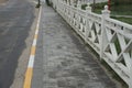 A long alley of gray paving slabs by an asphalt road along a white wooden fence Royalty Free Stock Photo